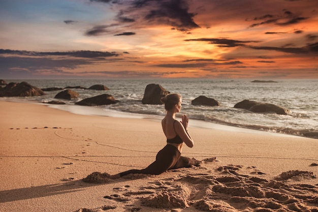 La posición de yoga de la mujer joven se divide o se enrosca para un estilo de vida saludable en el mar tropical o en la playa del océano al aire libre