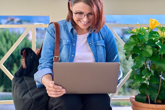 Positiv lächelnde Geschäftsfrau mittleren Alters mit Laptop im Freien