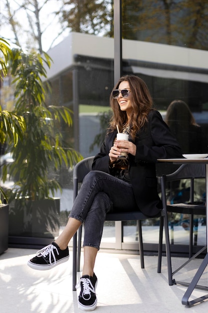 Positiv lächelndes Mädchen mit Sonnenbrille sitzt an einem Tisch auf der Straße in einem Café Selbstbewusste Frau