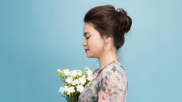 Positiv von junger Frau mit dunklen Haaren hält hübsch Bouquet lächelte sanft isoliert über blauen Hintergrund