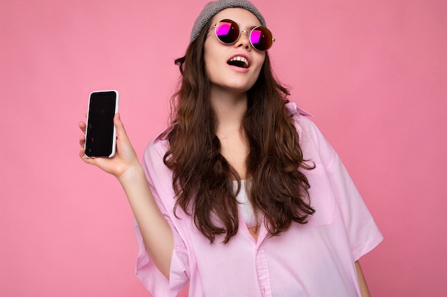 Positiva atractiva joven morena vistiendo elegante camisa rosa, sombrero gris y colorido