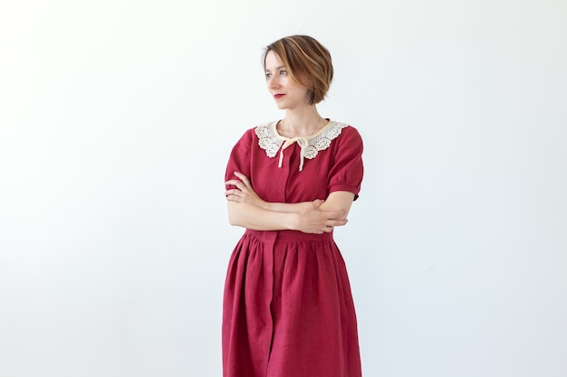 Positiva bela jovem sorridente posando em vestido modesto de parede branca vermelha. Conceito de uma jovem elegante.