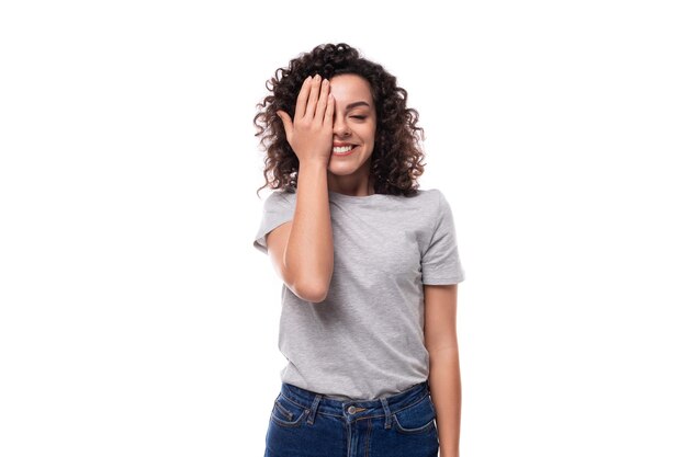 Positiva confiada brillante joven europea delgada mujer morena con estilo de cabello rizado vestida de gris