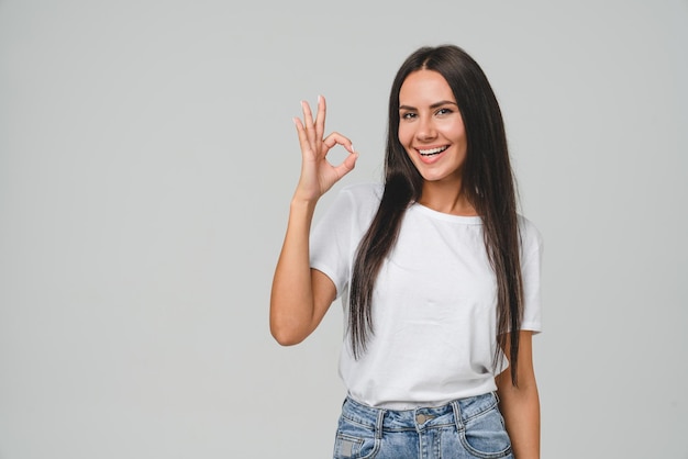 Positiva jovem caucasiana mulher de camiseta branca mostrando bom gesto olhando para a câmera verificando boa qualidade recomendação isolada em fundo cinza bem feito ótimo trabalho