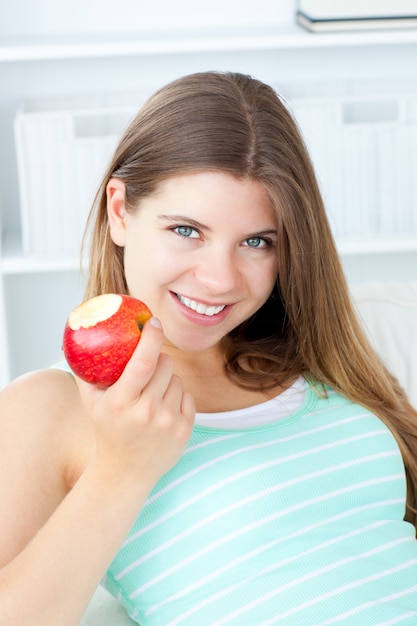 Positiva mulher comendo uma maçã sorrindo para a câmera