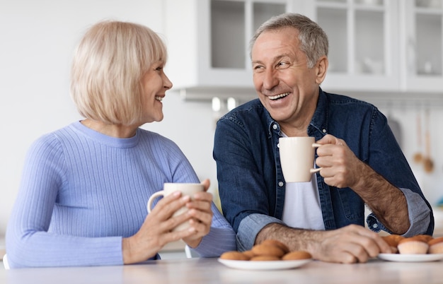 Positive ältere Ehepartner, die zu Hause Tee mit Gebäck trinken