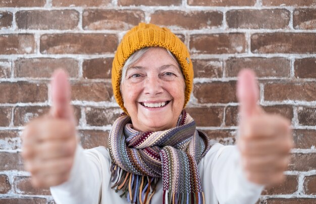 Positive ältere Frau mit Daumen hoch lächelnd in die Kamera schaut - Backsteinmauerhintergrund
