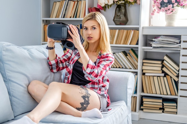 Positive blonde Frau, die sich auf einem Sofa entspannt und ein Virtual-Reality-Brillengerät verwendet