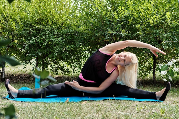 Positive blonde Frau führt Dehnübungen im Park durch. Fitness-Training im Freien