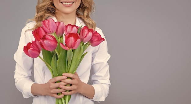 Positive blonde Frau mit Frühlingstulpenblumen auf grauem Hintergrund