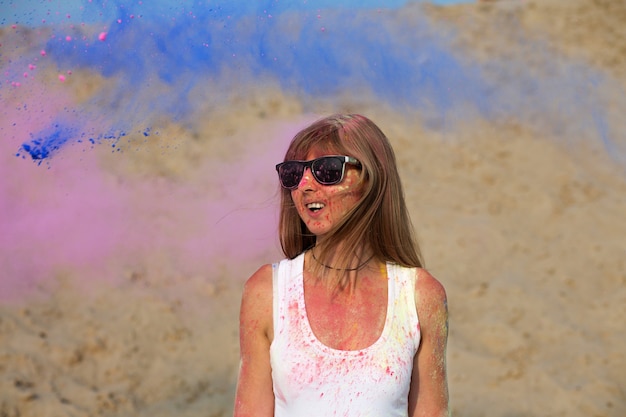 Positive blonde Frau mit Sonnenbrille, die das Holi-Festival in der Wüste genießt. Platz für Text