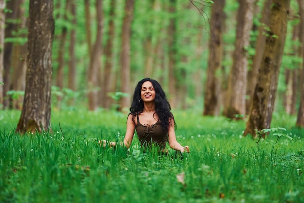 Positive Brünette in Freizeitkleidung, die tagsüber im Wald meditiert