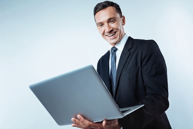 Positive Einstellung zur Arbeit. Low Angle Shot eines aufgeregten reifen Unternehmers, der einen Bildschirm eines Computers mit einem breiten Lächeln auf seinem Gesicht betrachtet, während er über dem Hintergrund arbeitet.