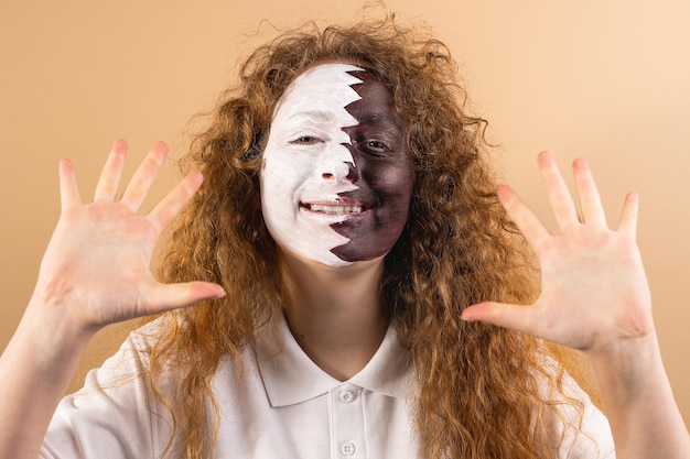 Foto positive fan-fußballfrau mit lächelndem bemaltem gesicht in katar-flagge, die ihre handflächen zeigt, die auf gelbem hintergrund in die kamera schauen hochwertiges foto