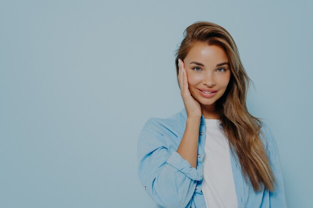 Positive Frau, die auf hellblauem Hintergrund in die Kamera lächelt