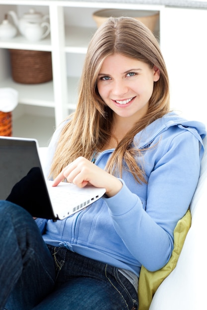 Positive Frau, die einen Laptop sitzt auf einem Sofa verwendet