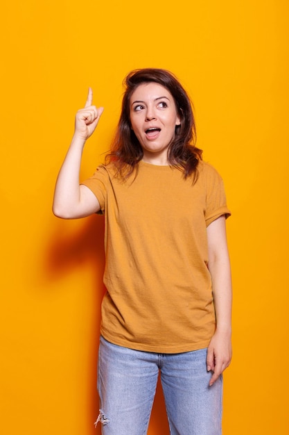 Positive Frau, die mit dem Zeigefinger nach oben zeigt und vor isoliertem Hintergrund steht. Kaukasischer Erwachsener, der nach oben zeigt und mit der Hand Gesten macht, um die Richtungen im Studio anzuzeigen.