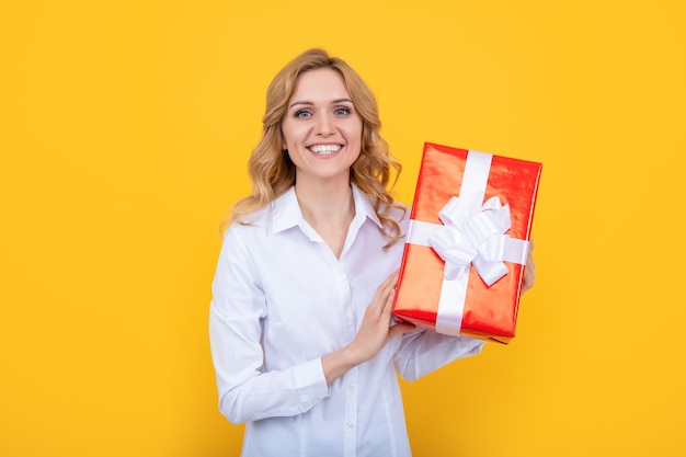 Positive Frau hält große Geschenkbox auf gelbem Hintergrund