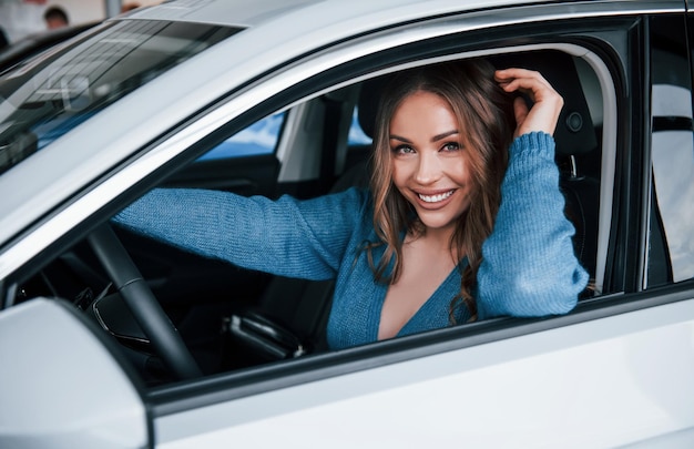 Positive Frau im blauen Hemd sitzt im neuen, brandneuen Auto im Autosalon oder Flughafen