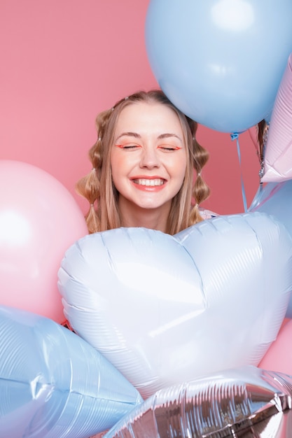 Positive Frau in Luftballons auf einer rosa Oberfläche