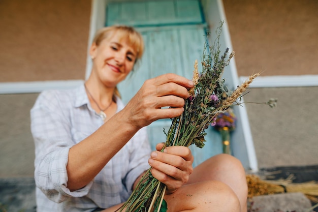 Positive Frau kreiert schöne Urlaubssträuße aus getrockneten Blumen mit einem Lächeln im Gesicht