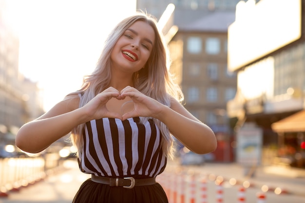 Positive Frau mit roten Lippen, die mit ihren Fingern Herzzeichen machen