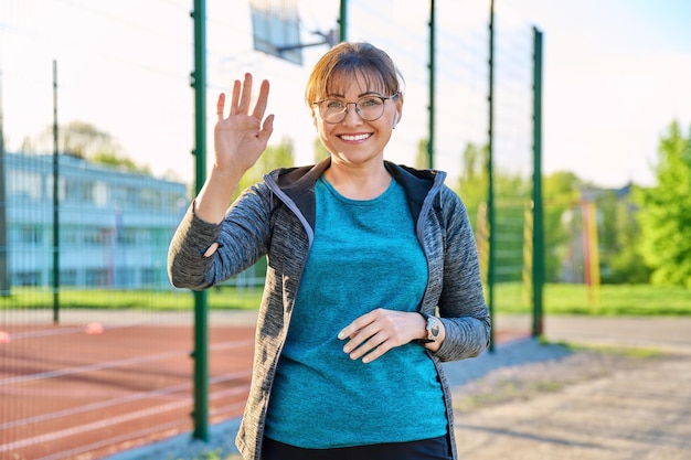 Positive Frau mittleren Alters, die in die Kamera schaut und mit der Hand winkt