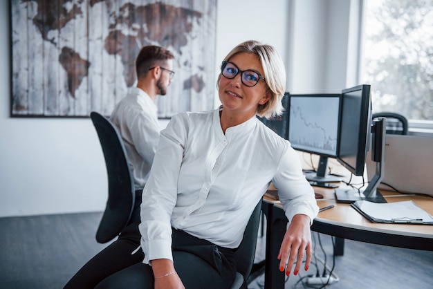 Positive Frau. Zwei Börsenmakler in formeller Kleidung arbeiten im Büro mit Finanzmarkt.