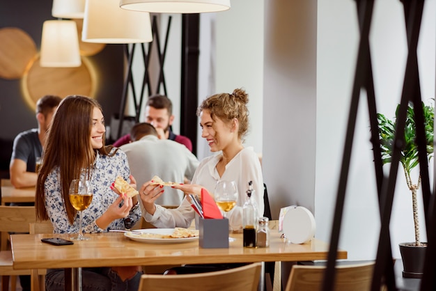 Positive Freundinnen, die in der Pizzeria plaudern und essen.