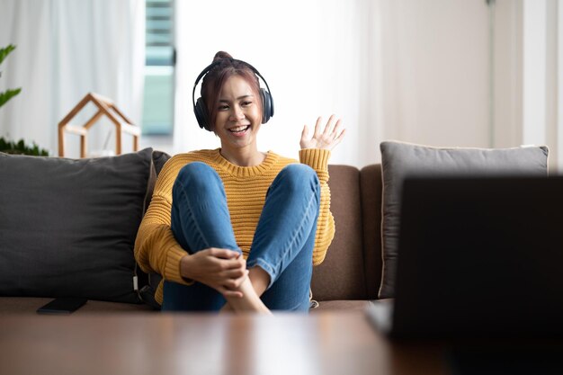 Positive fröhliche asiatische Mädchen haben Online-Videoanruf Sendung treffen Blogger sagen, hallo Welle Hand sitzen Tisch verwenden Laptop im Haus drinnen