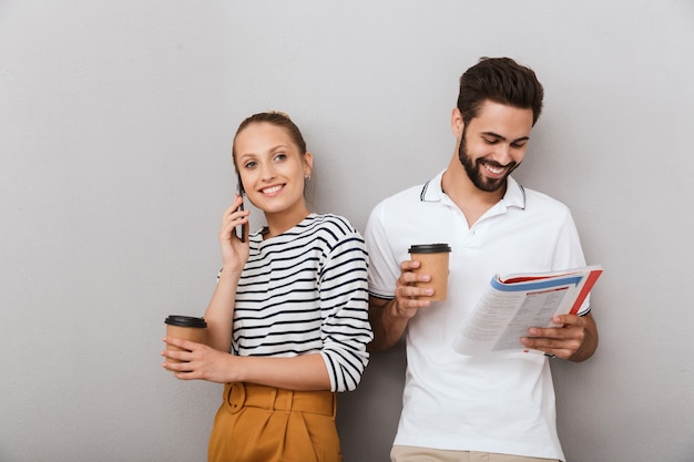 Positive fröhliche junge Liebespaar Freunde Mann und Frau drinnen isoliert über graue Wand sprechen per Handy mit Schreibheft.