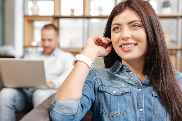 Positive Gefühle. Fröhlich entzückte attraktive Frau, die in ihrem Büro sitzt und lächelt, während sie in einer guten Stimmung ist