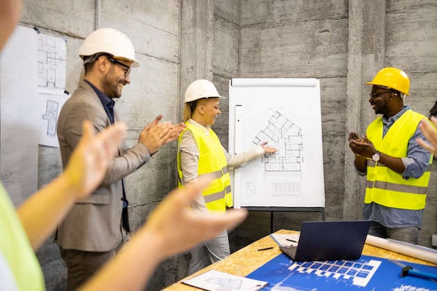 Positive Gruppe von Bauingenieuren auf der Baustelle, die sich lachend und klatschend in die Hände trifft