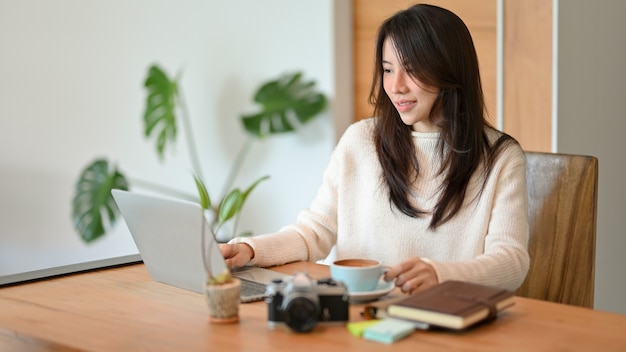 Positive junge Geschäftsfrau, die an einem Laptop zu Hause im Büro arbeitet