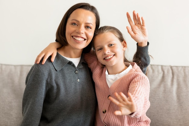 Positive kaukasische Tochter und Mutter mittleren Alters winken mit der Begrüßungsgeste und sagen „Hallo“ im Leben