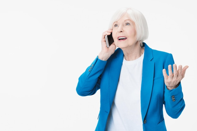 Positive lächelnde ältere Frau beim Sprechen am Telefon und aufgeregt lokalisiert über weißem Hintergrund