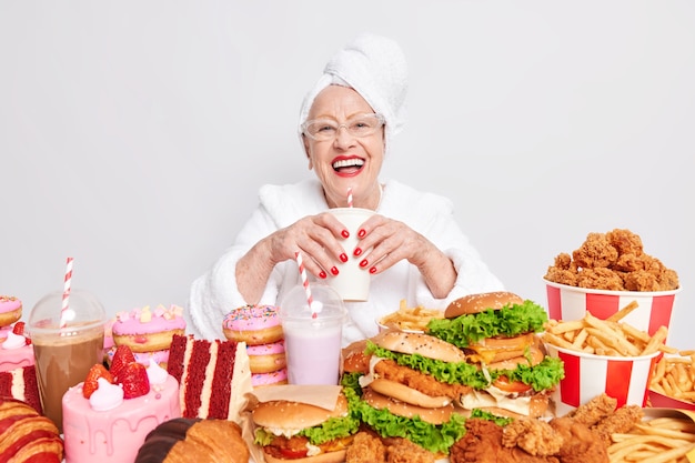 Positive sorglose Seniorin lächelt breit trinkt Limonade isst ungesundes Essen hat gute Laune