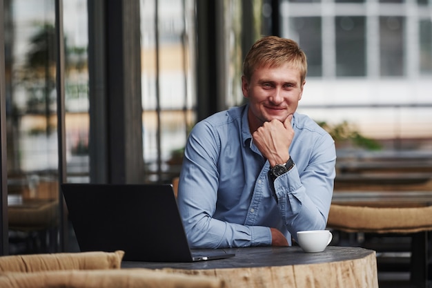 Positive Stimmung. Vorderansicht des Kerls, der tagsüber mit seinem Laptop in einem modernen Café ist.