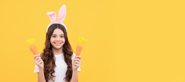 Positive Teenager-Mädchen in Hasenohren halten Karotte auf gelbem Hintergrund Ostern Ostern Kind horizontale Poster Web-Banner-Header von Bunny Kid Copy Space