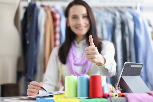 Positive weibliche Näherin im Atelier Daumen hoch Geste talentierte Schneiderin