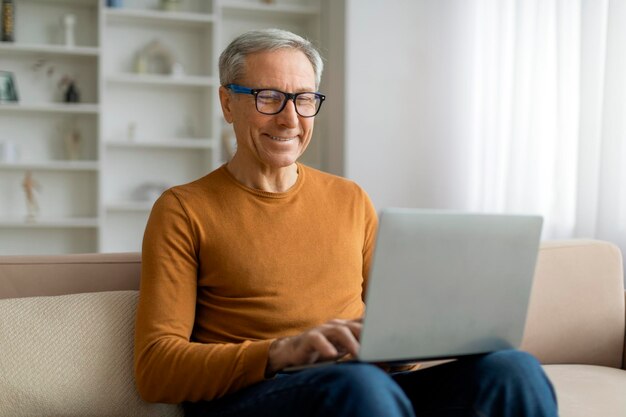 Positiver älterer Mann mit Brille, der zu Hause einen Laptop benutzt