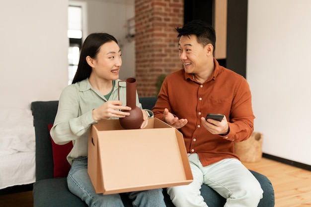 Positiver asiatischer Ehemann und Ehefrau, neue Eigentümer, Mieter der Wohnung, die nach dem Umzug auspacken