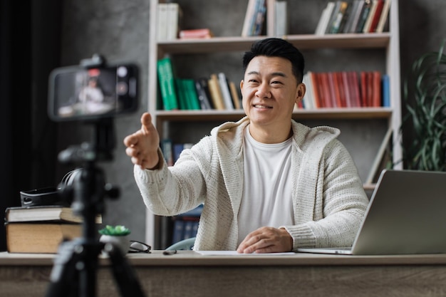 Positiver asiatischer Mann in Freizeitkleidung, der mit ausgestreckter Hand zur Begrüßung in die Kamera blickt