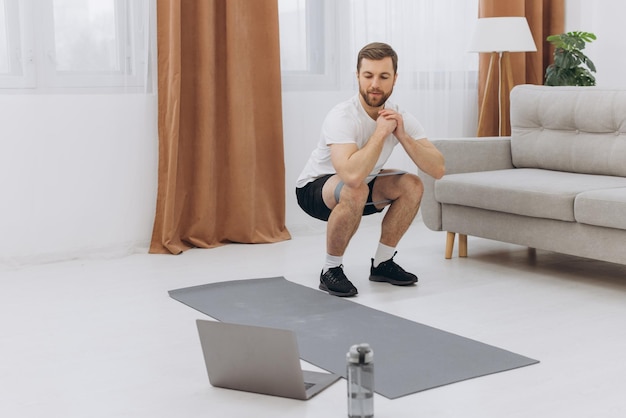 Positiver athletischer bärtiger Mann mittleren Alters, der sich zu Hause mit einem Laptop ausdehnt, der Sportvideos im Internet anschaut und einen Online-Kopierbereich für Fitnesskurse hat Gesunder Lifestyle-Sport auf Selbstisolierung