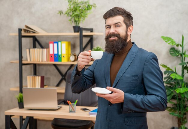 Positiver bärtiger Geschäftsmann trinkt Kaffee im Büro mit Kopierraum am Morgen