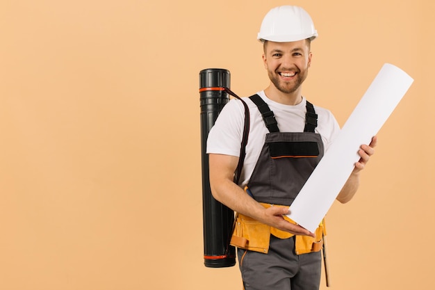 Positiver Bauingenieur untersucht eine Zeichnung und hält ein Rohr auf beigem Hintergrund