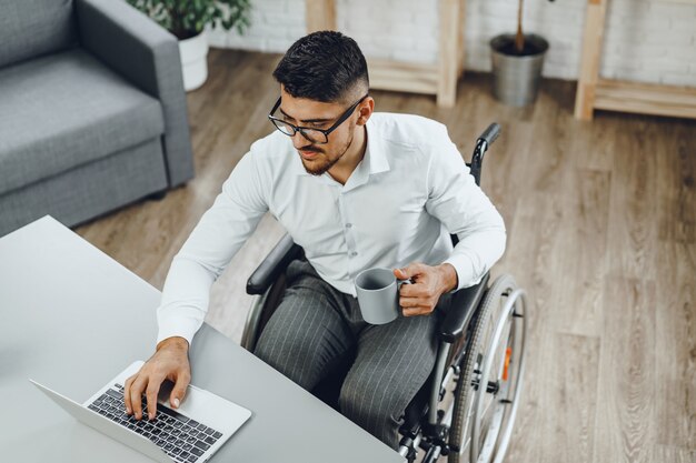 Positiver behinderter junger Mann im Rollstuhl, der im Büro arbeitet