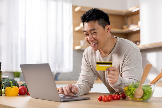Positiver chinesischer Mann, der Lebensmittel online kauft und zu Hause kocht