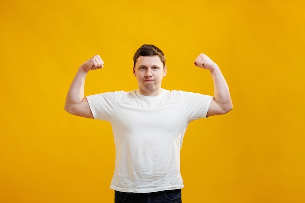 Positiver emotionaler Mann lächelt, zeigt Muskeln an seinen Armen, fühlt sich stolz darauf, stark zu sein und Kraft zu haben, sagt, ich bin Held. Muskulöser männlicher Athlet hebt vor Freude die Arme, zeigt, wie stark er ist