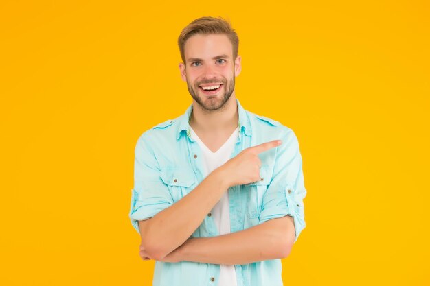 Positiver glücklicher Kerl, der mit dem Finger zeigt und Jeans-Outfit auf gelbem Hintergrund trägt, der das Produkt präsentiert